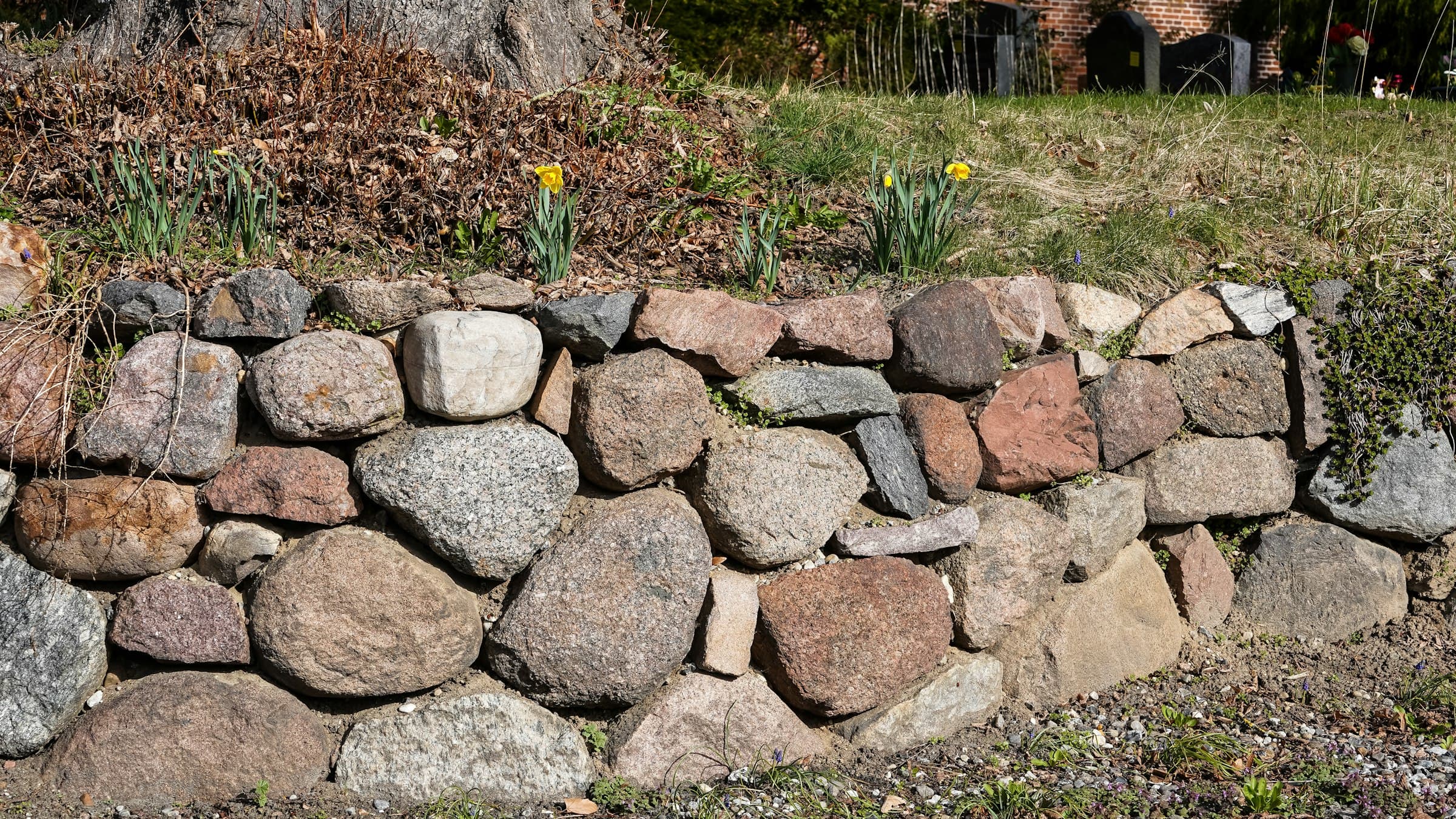 Backyard stone patio with a low retaining wall and landscape lighting at dusk